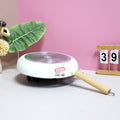 Small frying pan with wooden handle on a white surface against a pink wall.