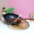 Black wok with wooden handle on a white surface with pink background