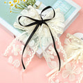 White lace bow with a black ribbon on a pink background