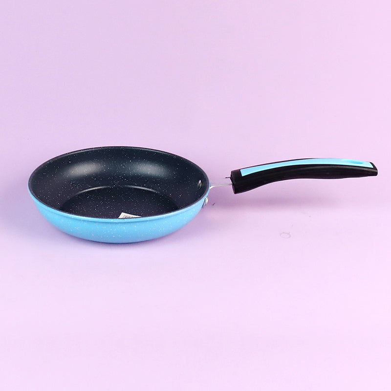 Blue frying pan with black speckled interior on a light purple background