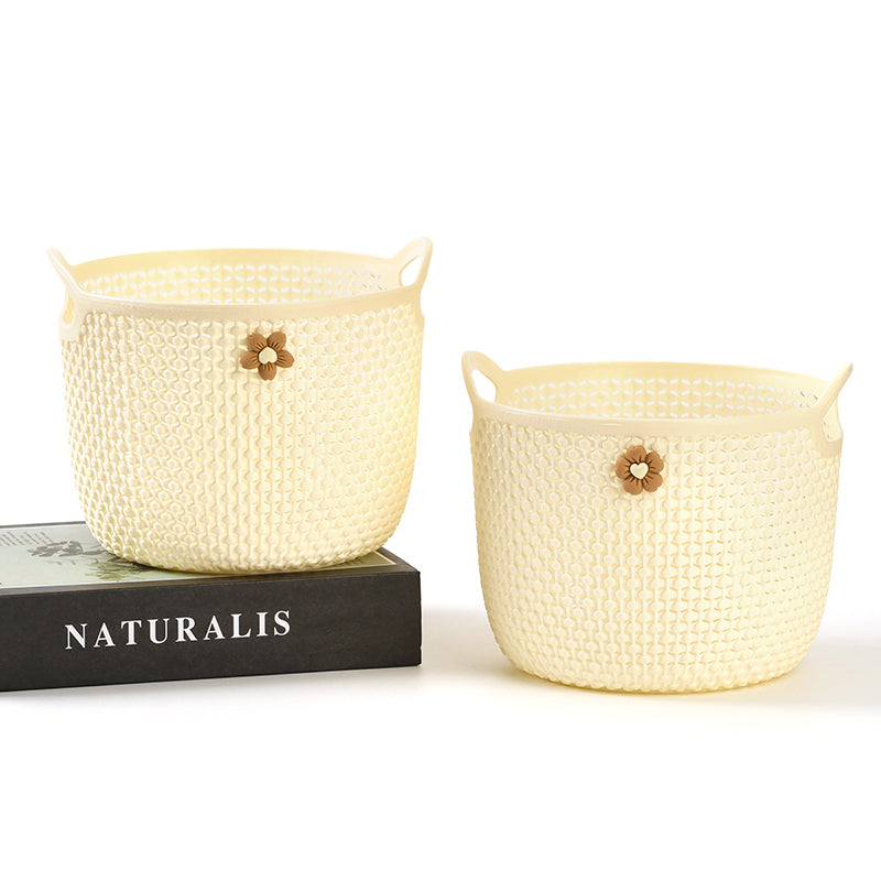 Two cream-colored woven baskets with floral accents on a white background, one on top of a black book titled 'NATURALIS'.
