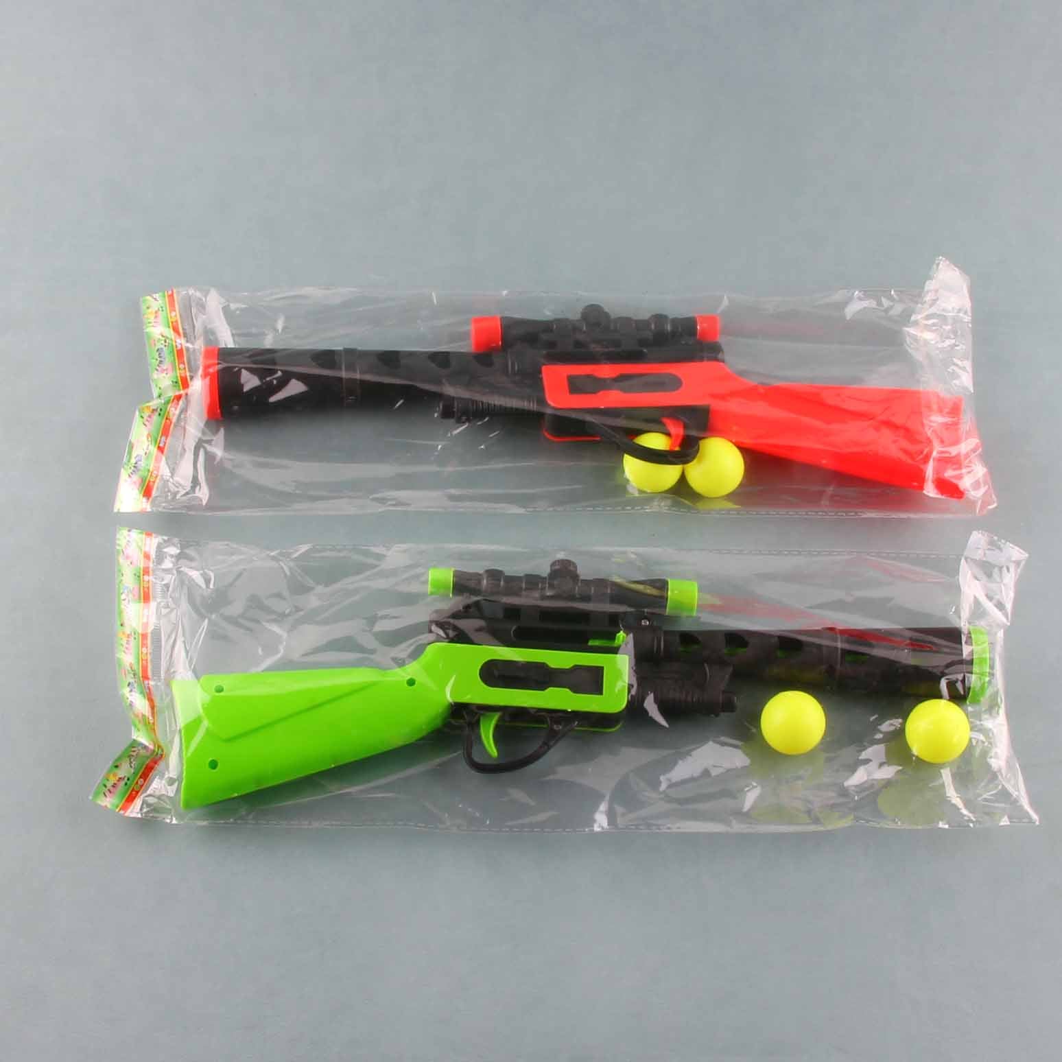 Two toy guns, one red and black, one green and black, with yellow balls on a gray background.